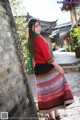 A woman in a red shirt and a colorful skirt.