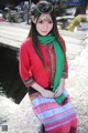 A woman in a red shirt and green scarf sitting on a stone wall.