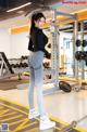 A woman in a black top and gray leggings standing in a gym.