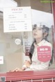 A woman sitting in front of a store window with a price list.