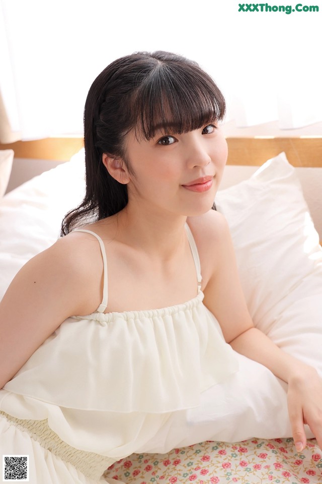A woman in a white dress sitting on a bed.