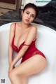 A woman in a red lingerie sitting in a bathtub.