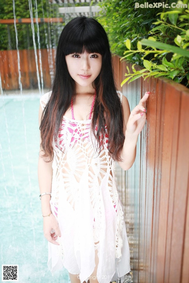 A woman in a white dress standing next to a pool.