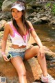 A woman sitting on a rock next to a stream.