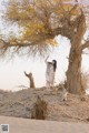 A woman standing in front of a tree in the desert.