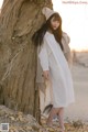 A woman leaning against a tree on the beach.