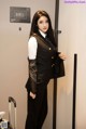 A woman in a black suit standing next to a door.