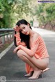 A woman in an orange dress crouching down on the road.