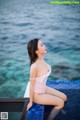 A woman in a white bathing suit sitting on the edge of a pool.