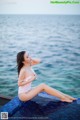 A woman in a white bathing suit sitting on the edge of a swimming pool.