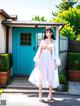 A woman in a white dress standing in front of a blue door.