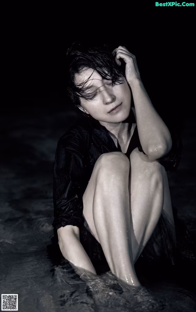 A woman sitting in the water with her head in her hands.