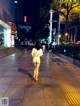 A woman walking down a sidewalk at night. 