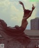 A naked woman in a long skirt is dancing on a rooftop.