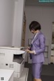 A woman in a purple suit standing next to a printer.