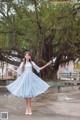 A woman in a blue dress standing in front of a tree.