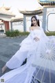 A woman in a white dress sitting on the ground with an umbrella.