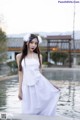 A woman in a white dress standing by a pool.